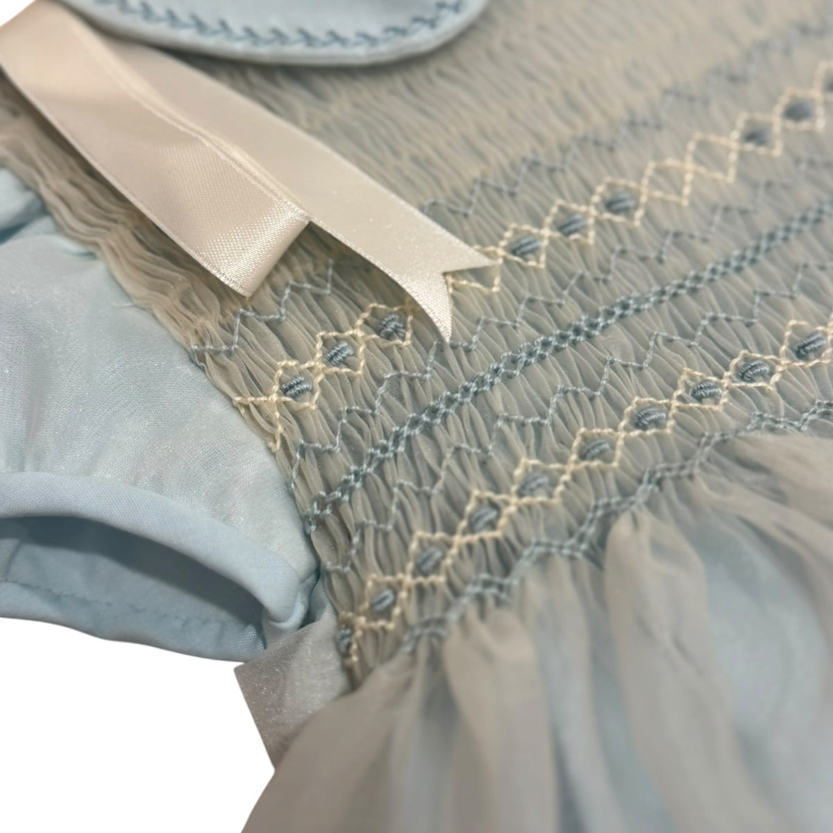 Close-up of ivory ribbon and smocked detailing on Agustin Light Blue Romper