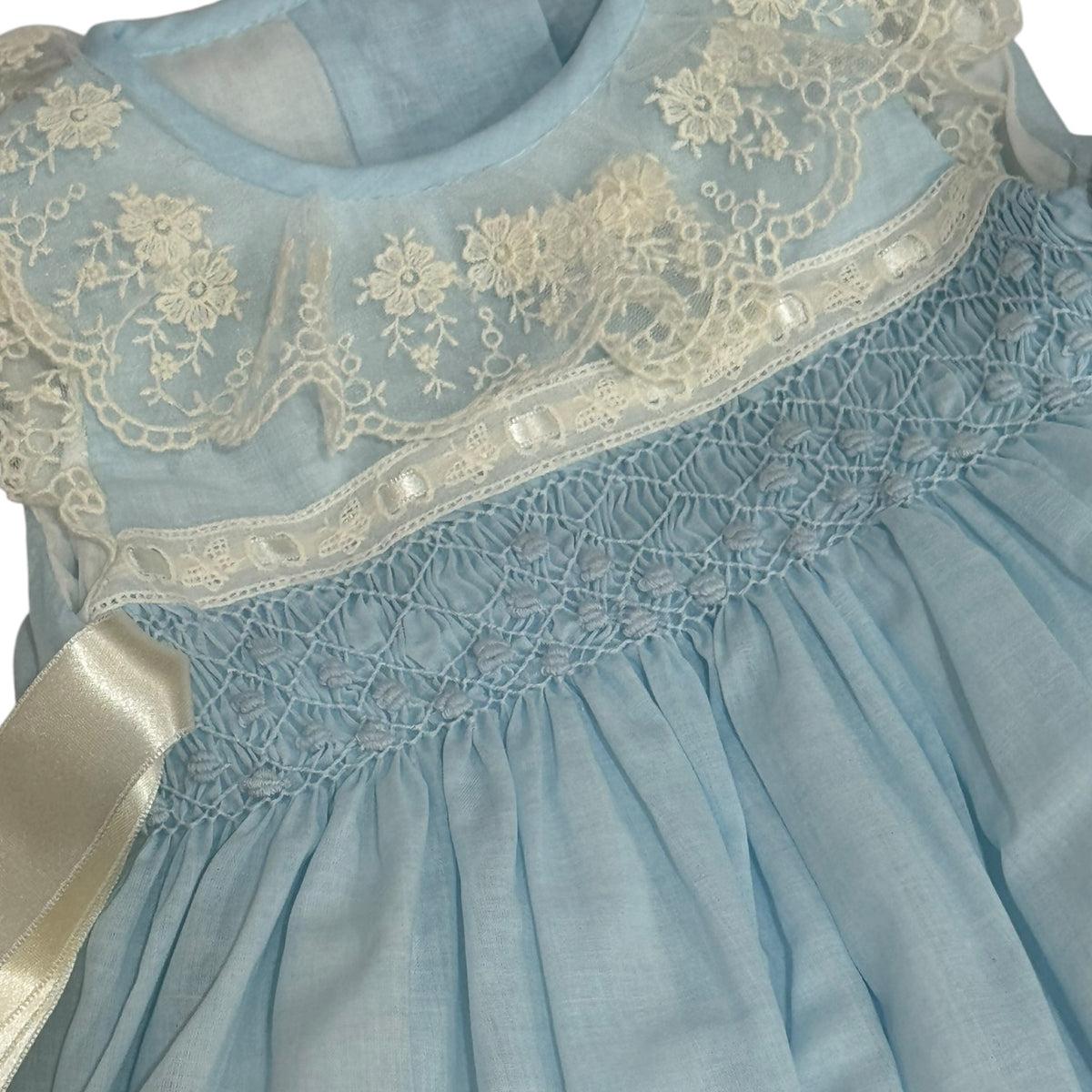 Close-up of intricate light blue handsmocking and ivory lace on Helena Heirloom Romper