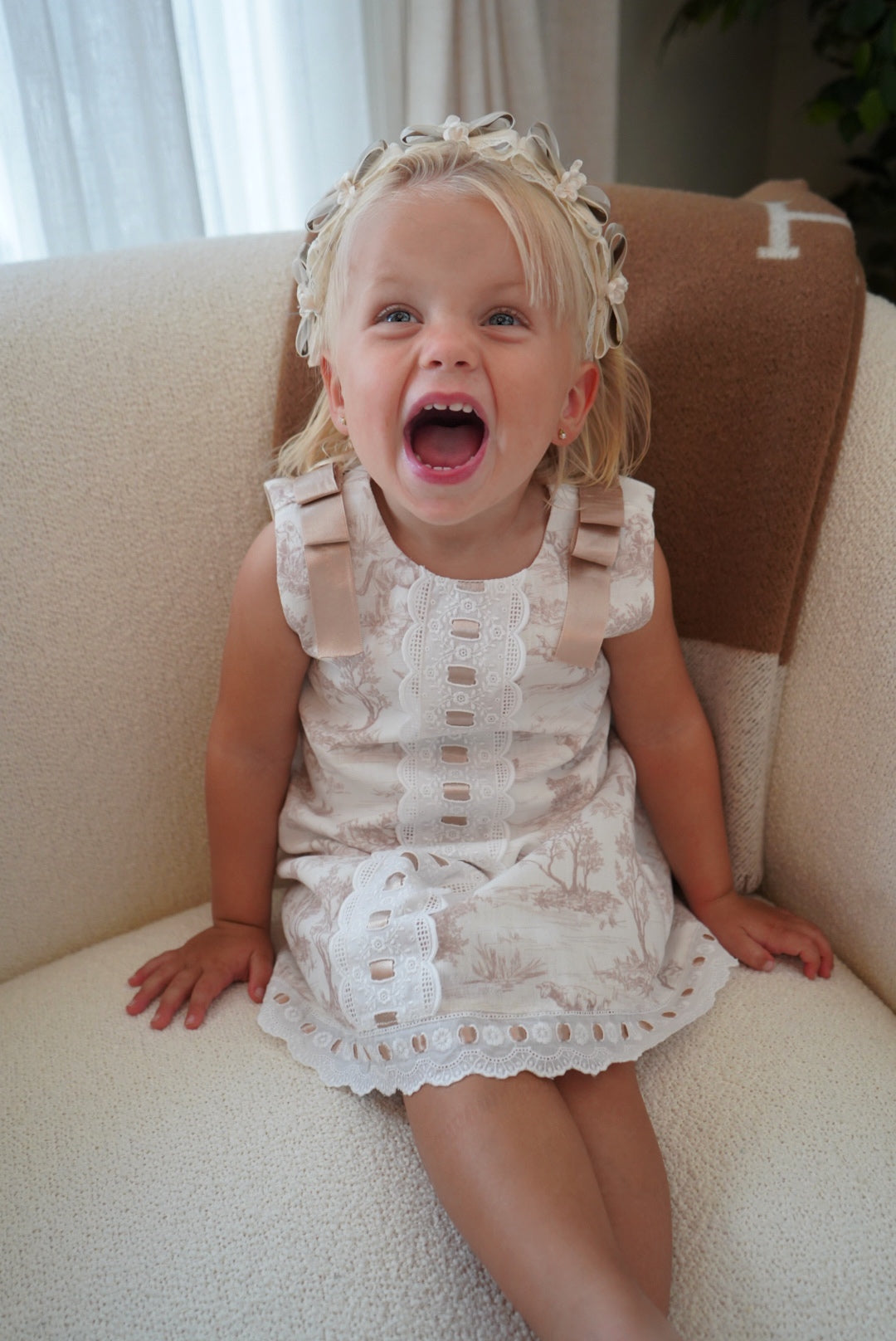 Girl seated in TPWC Toile Beige Ribbon Dress with ivory lace detailing