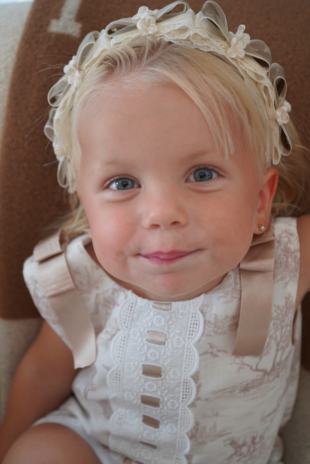 Girl wearing beige toile dress with satin ribbon shoulder bows
