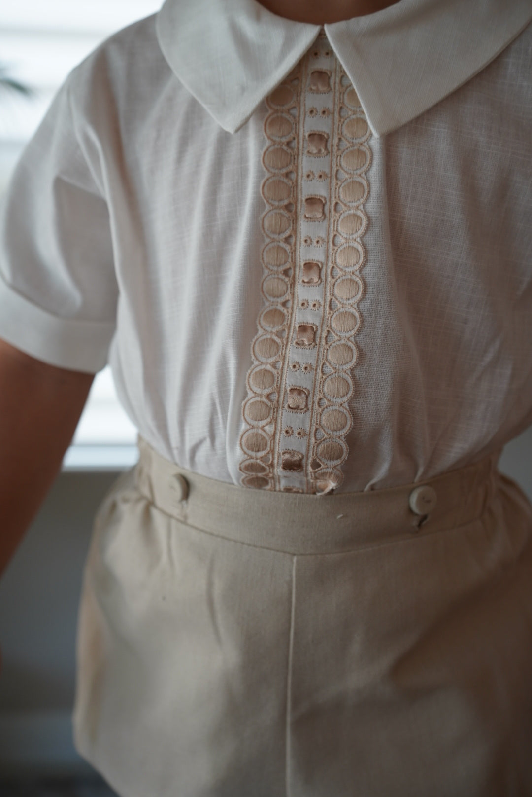 Close-up of ivory shirt and beige bloomer shorts from two-piece boy set